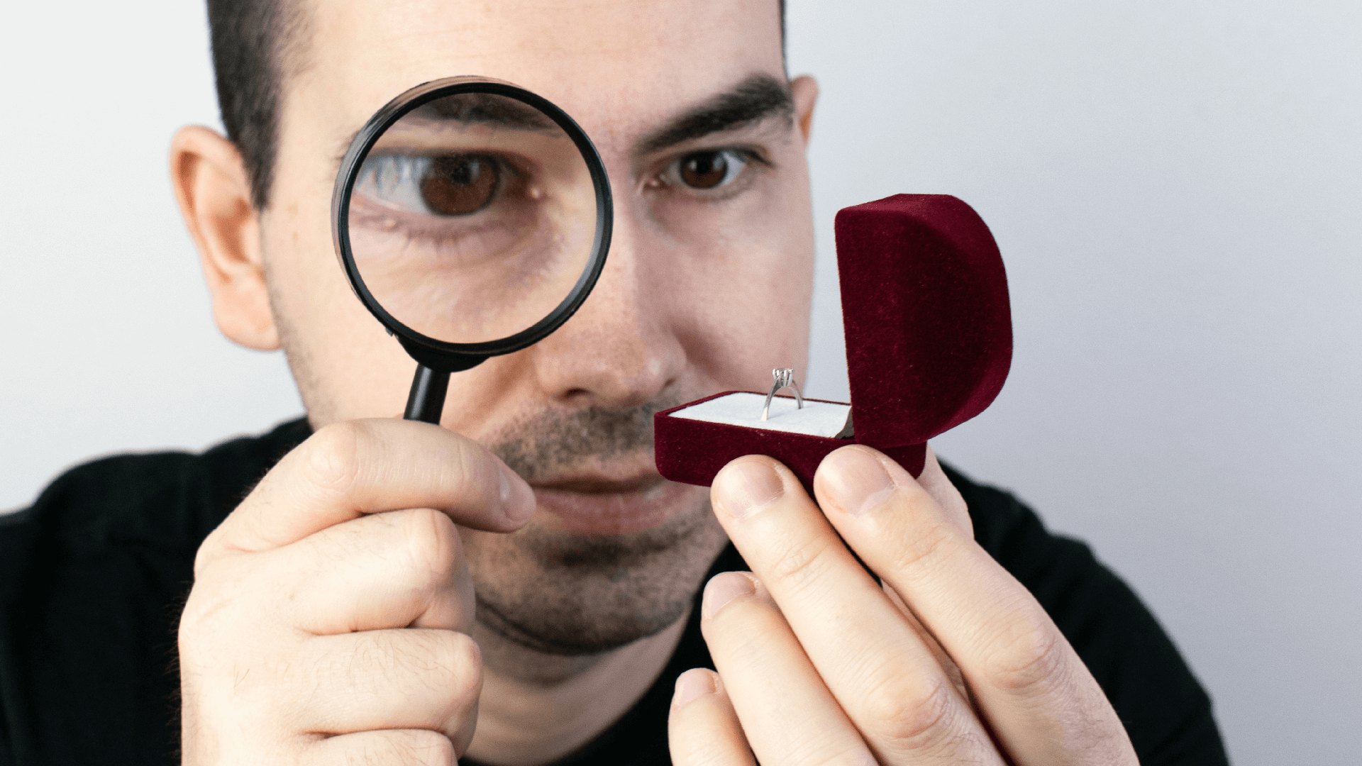 a man examines a diamond engagement ring in a ring box with a magnifying-glass