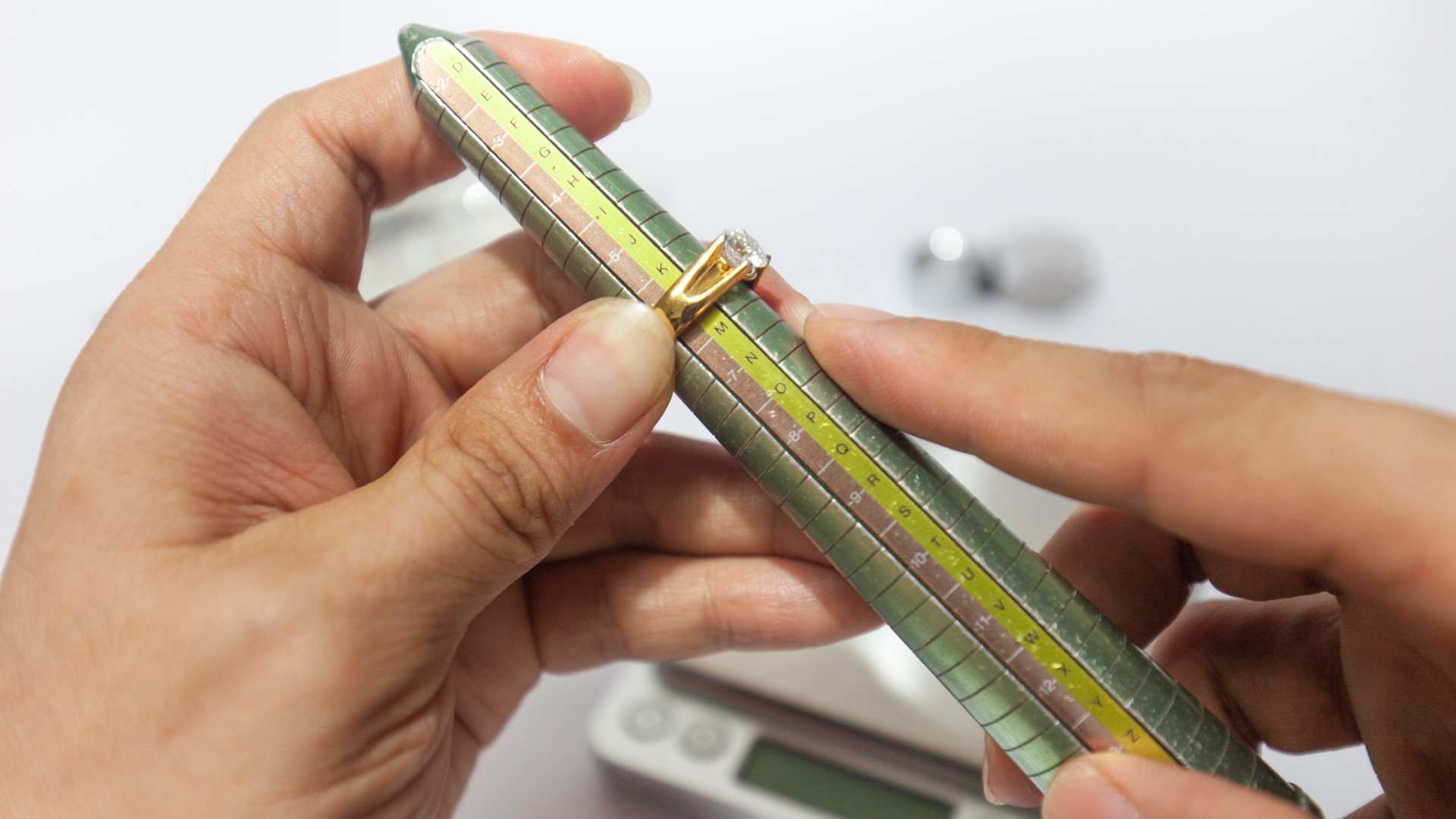 two hands are measuring a ring on a ring sizer gauge