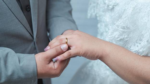 a groom puts a wedding band on a bride’s finger