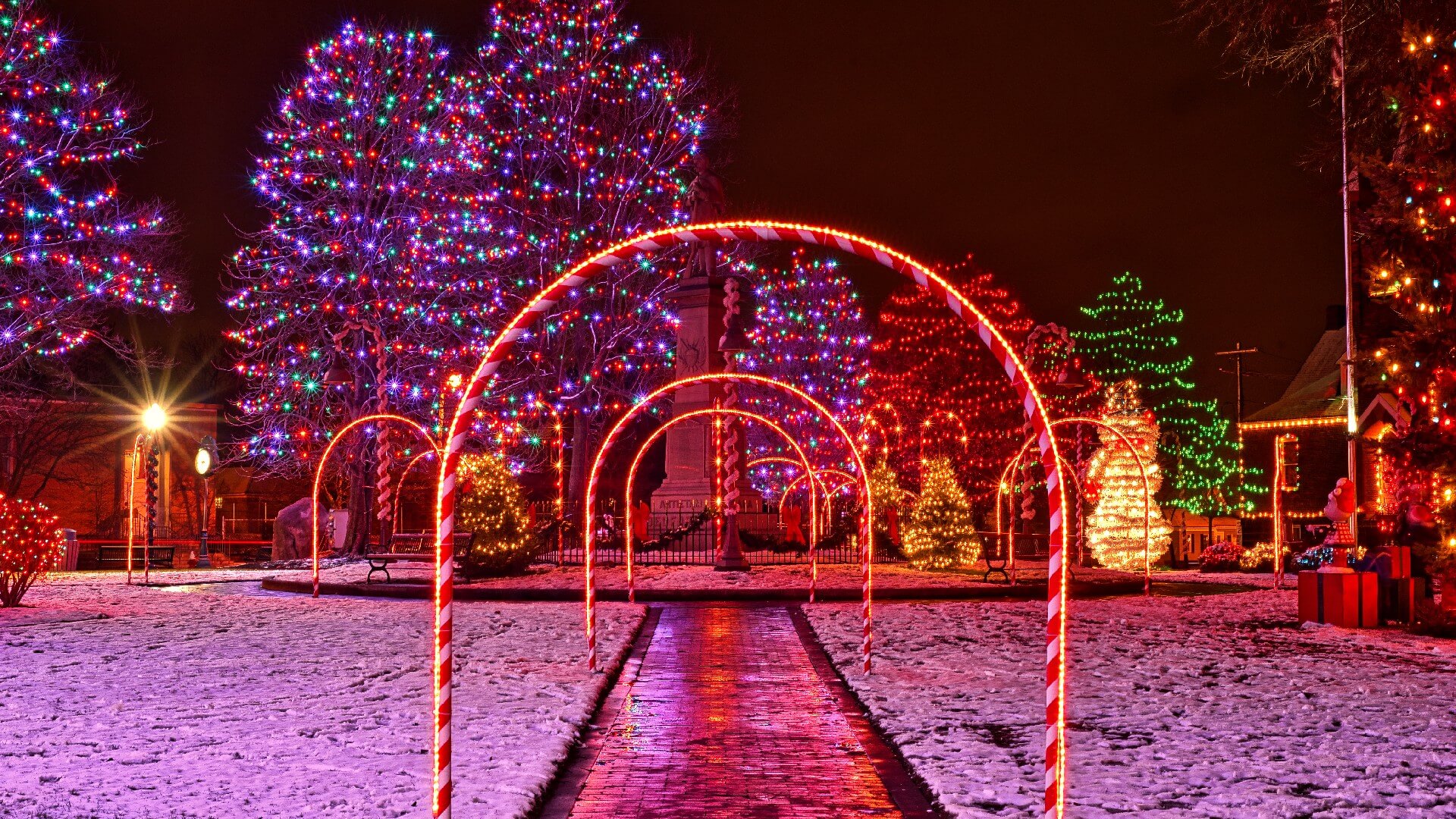 a festive Christmas display on  village commons with lighted archways over brick paths, tree lights, and a snowman